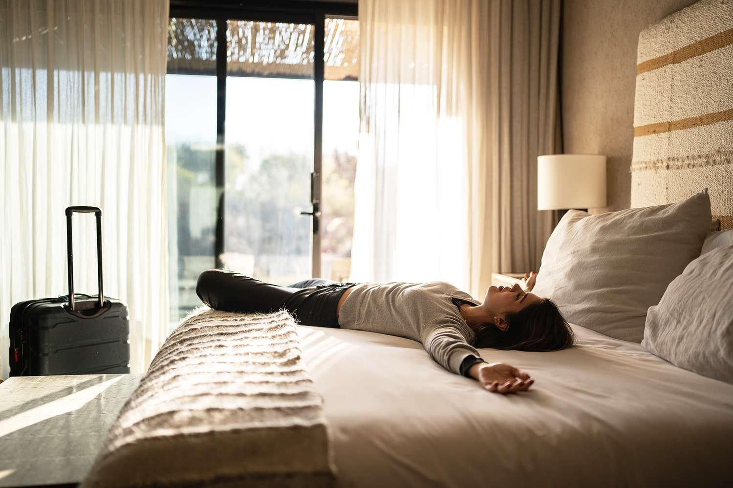 A tired traveler resting on a plush bed at Hotel Parkhills to recover from jet lag in a sunlit room